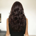 Woman with long, wavy dark brown wig from behind in a neutral setting