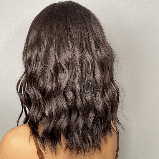 Back view of a person with wavy brown wig on a plain background
