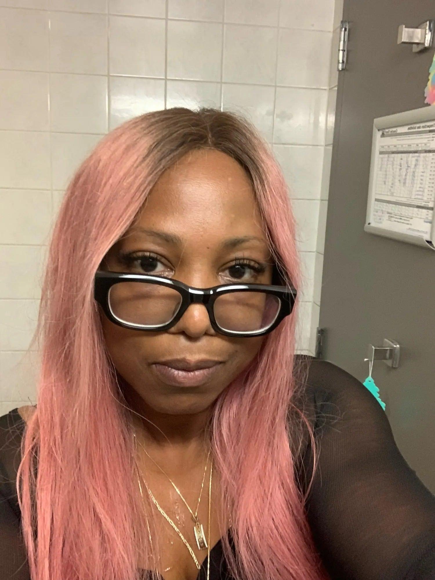Person with pink hair and glasses in a bathroom setting