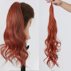 Reddish-brown hair ponytail extension on a mannequin head and held by a hand against a white background.