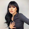 Woman with black wig with bangs and stylish makeup wearing a dark outfit against a plain background