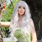 Woman with long white hair wig  and a green dress standing outdoors.
